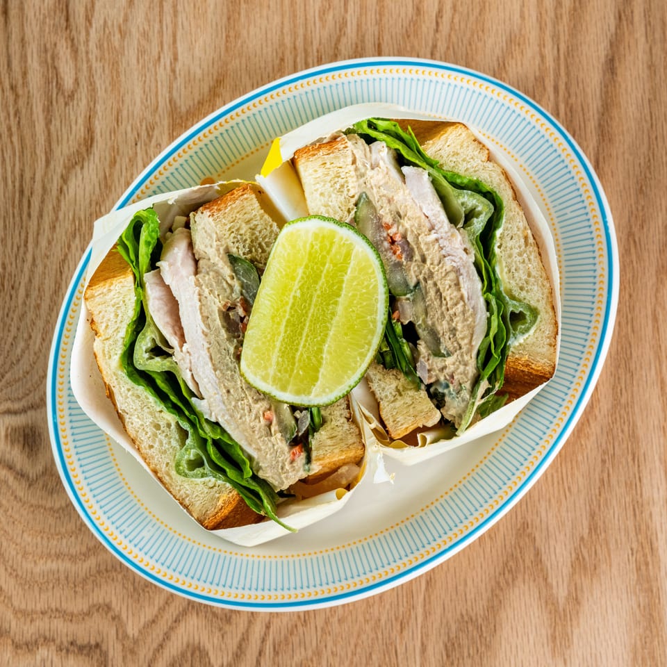 Overhead view of sliced chicken salad sandwiches with lettuce, cucumber, and lime on a patterned plate.