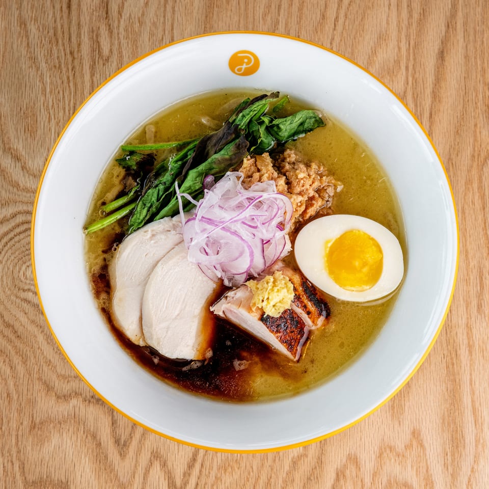 Bowl of ramen topped with sliced pork, grilled meat, greens, red onion, crispy garnish, and a soft-boiled egg.