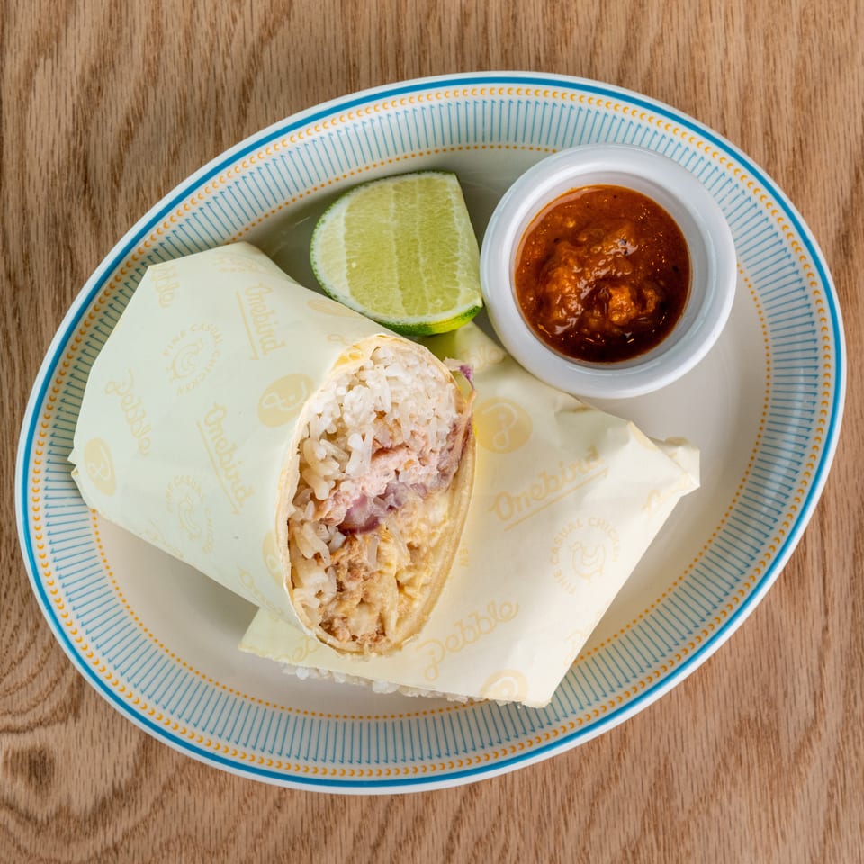 Top-down view of a rice-filled burrito on a patterned plate with lime wedge and red salsa on a wooden table.