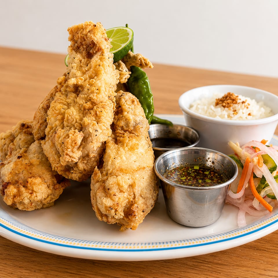 Crispy fried chicken drumsticks with lime, rice, pickled vegetables, and dipping sauces on a plate.