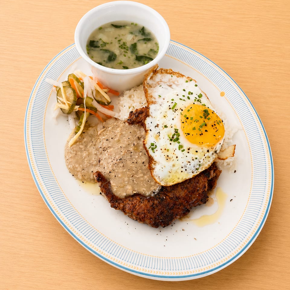 Crispy fried pork chop with gravy, rice, fried egg, pickled vegetables, and a side of soup.