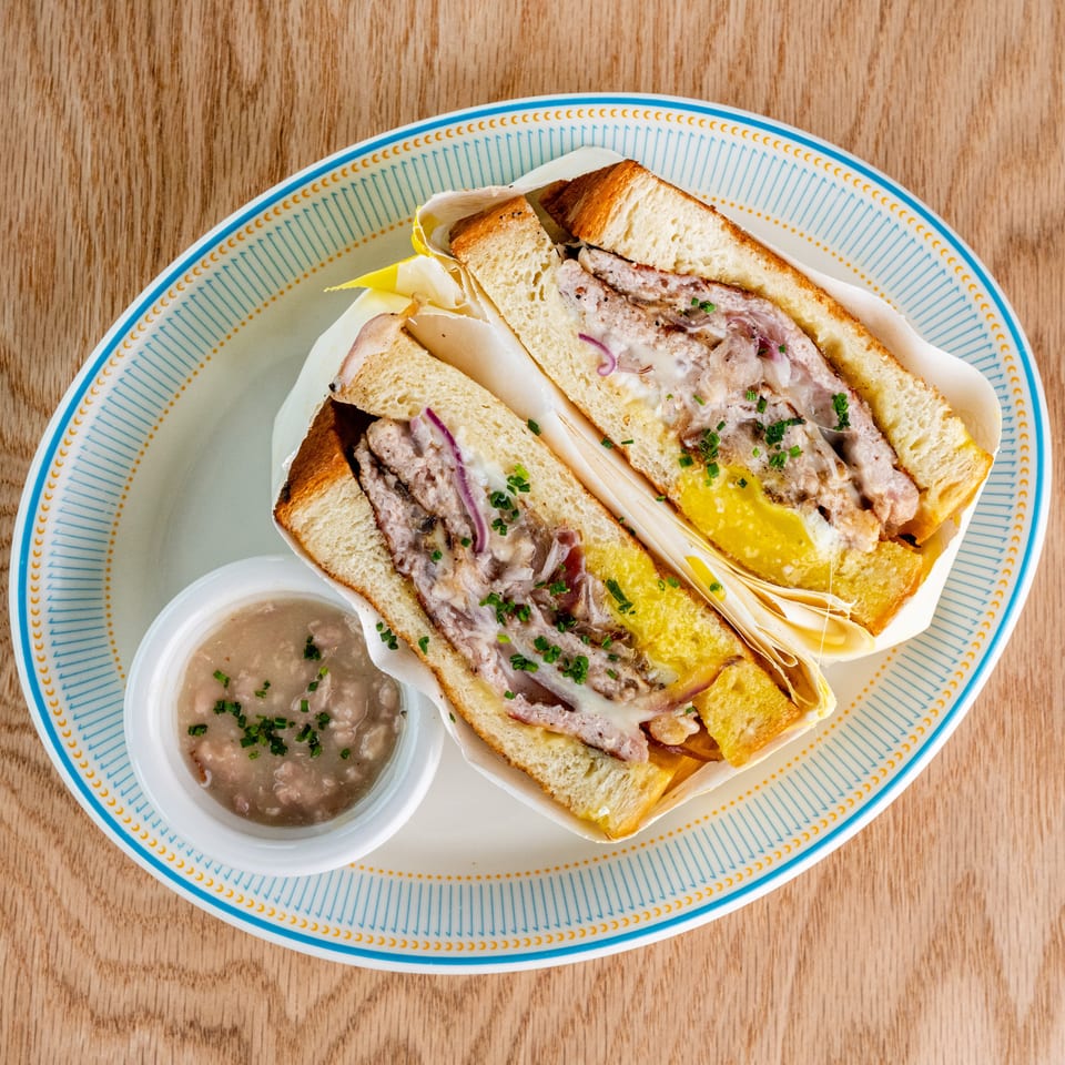 Two toasted sandwiches with meat, melted cheese, onions, and herbs served with dipping sauce on a patterned plate.