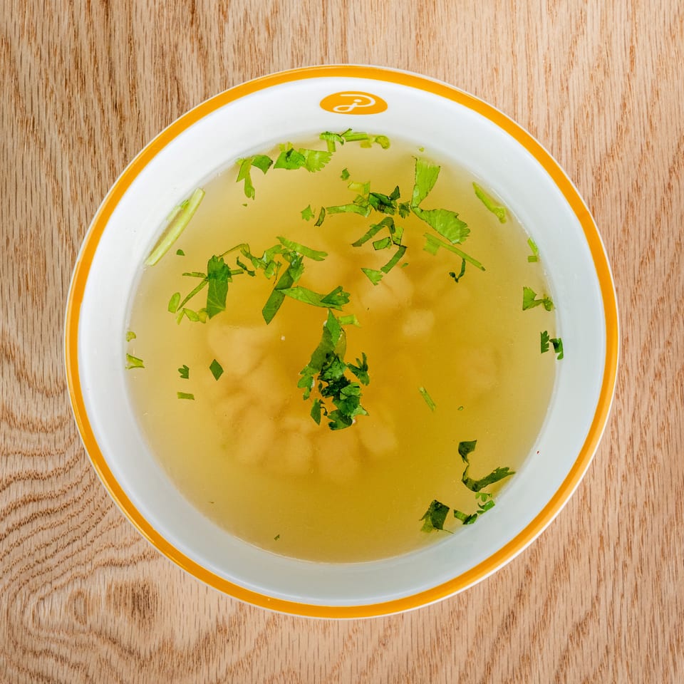Bowl of clear golden broth garnished with fresh cilantro on a wooden tabletop.