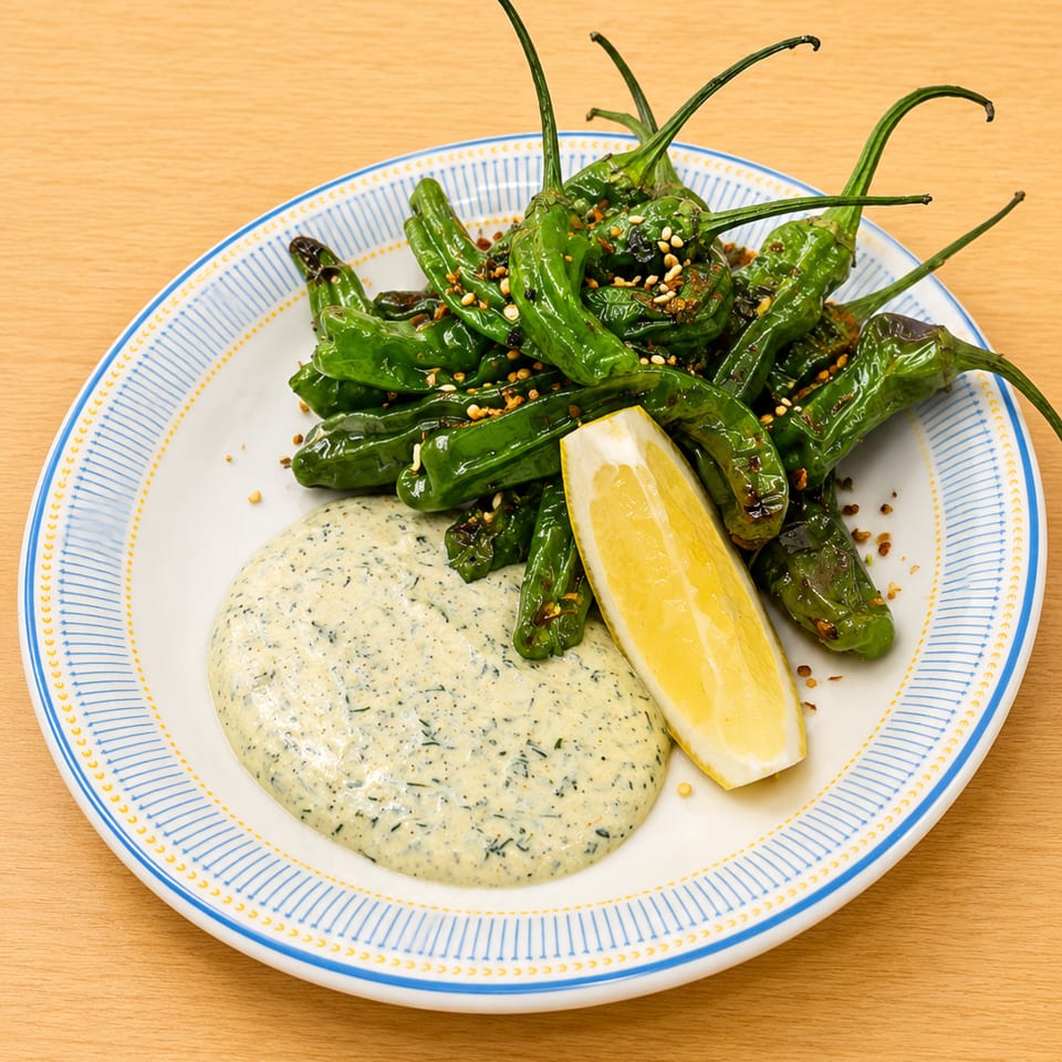 Plate of roasted green peppers with a creamy sauce, lemon wedge, and spices.