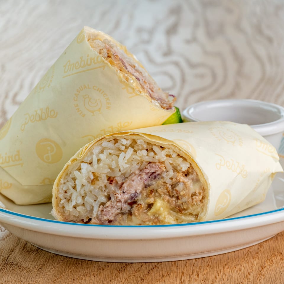 Sliced rice-filled wraps with meat and vegetables on a plate, accompanied by dipping sauce and branded wrapping.