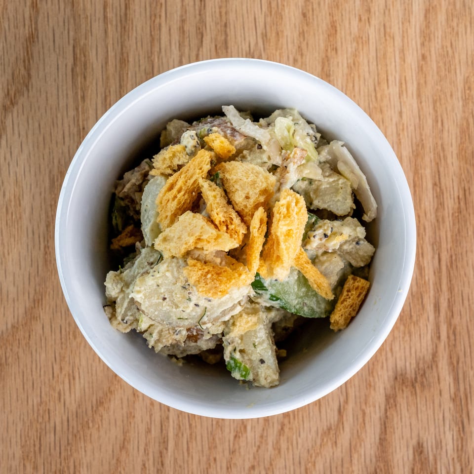 Bowl of creamy salad topped with golden crispy bread pieces on a wooden table.