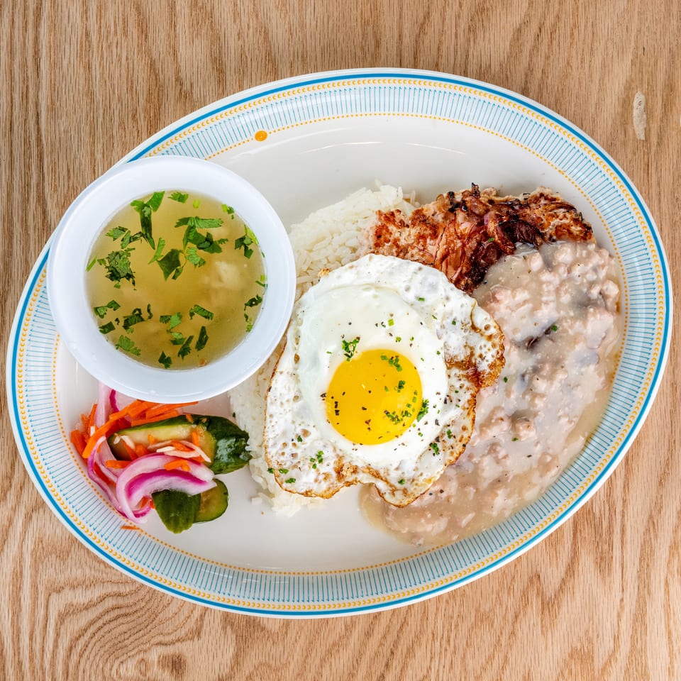 Vietnamese-style plate with rice, grilled pork, fried egg, creamy sauce, pickled vegetables, and herb-garnished broth.