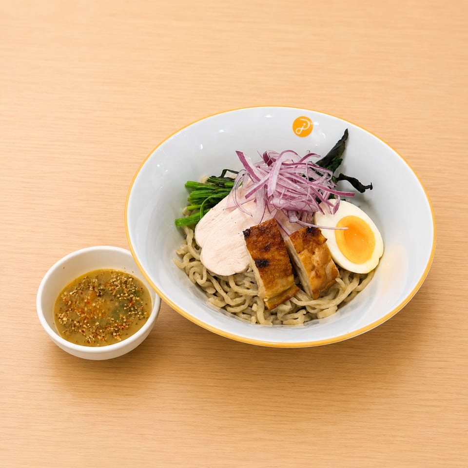 Ramen bowl with noodles, sliced chicken, grilled chicken, soft-boiled egg, red onions, and greens.