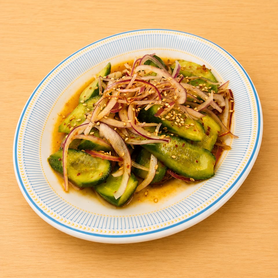 Cucumber salad with red onion, sesame seeds, and a savory dressing on a white and blue plate.