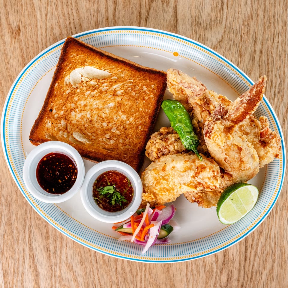 Crispy fried chicken with toast, sauces, pickled vegetables, lime, and a green pepper on a patterned plate.