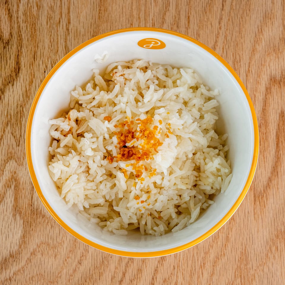 Overhead view of steamed white rice topped with orange seasoning in a white bowl with an orange rim on a wooden table.